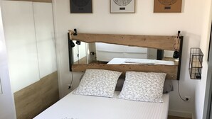 Un lit avec une tête de lit en bois, deux oreillers et un matelas. Trois tableaux encadrés sont accrochés au mur au-dessus du lit.