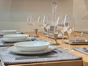 Une table à manger dressée avec de l’assiette blanche, des bols et des verres à vin transparents, agrémentée de sets de table à motifs et d’un centre de table décoratif.