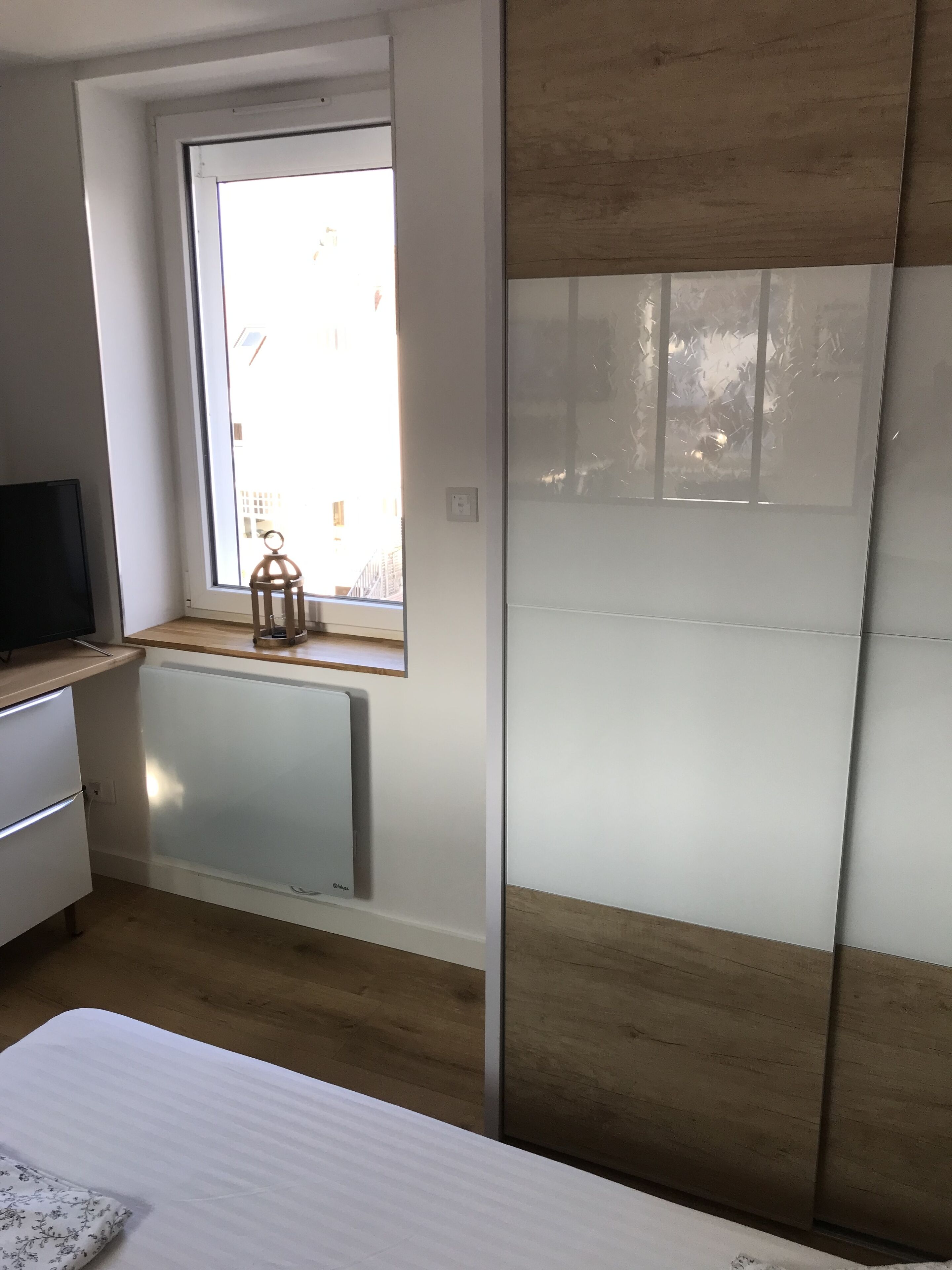 A bedroom with a window, a radiator, a bed, and a dresser.
