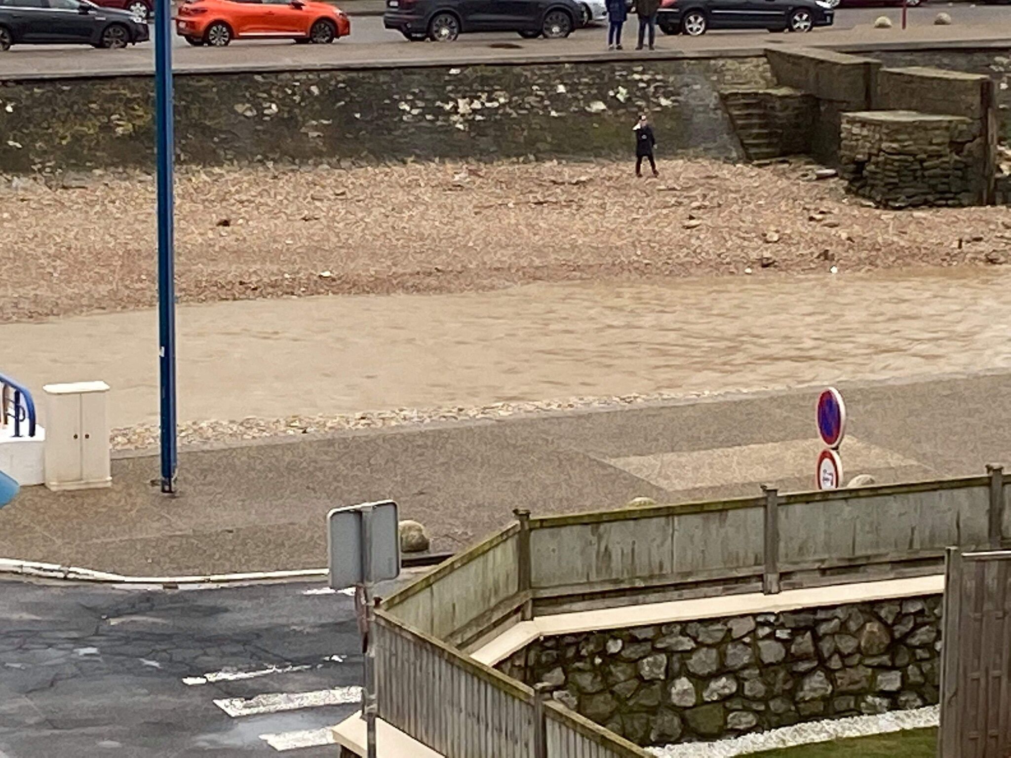 Une vue de rue avec un passage piéton, un mur de pierre et un panneau indiquant qu’il est interdit de se garer.