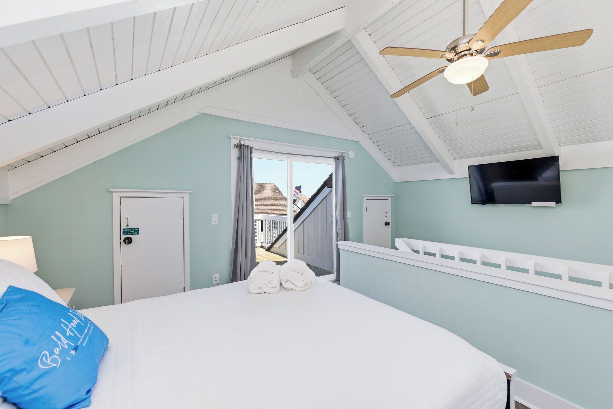 Een slaapkamer met een bed, een plafondventilator, een televisie en uitzicht op buiten.