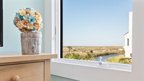 Une salle de bain avec un meuble-lavabo en bois, un vase de fleurs et une vue sur une rivière et des marais.
