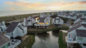 A residential area with houses featuring gabled roofs and front porches, a small waterway, and a view of the ocean.
