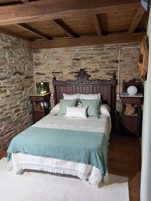 A rustic bedroom with a stone wall, a wooden bed with a carved headboard, and a small bedside table with a lamp. - Tourist use housing (Lugo)