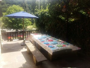 An outdoor dining area with a long table covered in colorful plates, benches, and a blue umbrella. - Tourist use housing (Lugo)
