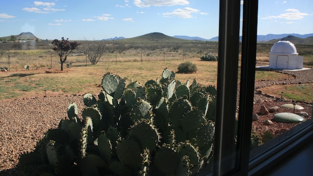 Un paysage désertique avec un cactus au premier plan et une structure en forme de dôme à l’arrière-plan.
