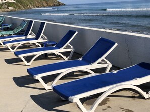 A row of blue and white sun loungers on a concrete deck overlooking the ocean.