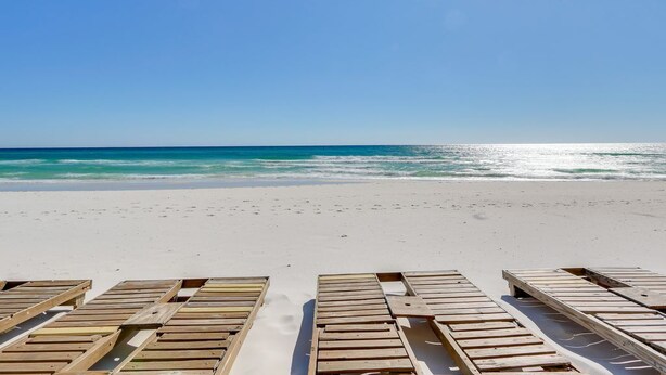 A beach with wooden lounge chairs facing the ocean. - Tropic Winds 1402 (Beachfront) - Free BeachService!! (Panama City Beach)