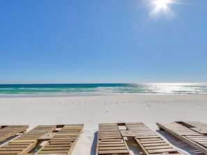 A beach with wooden lounge chairs facing the ocean.