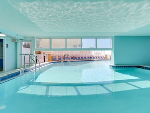 An indoor swimming pool with clear blue water, a 4 ft depth marker, and a view of a fenced area outside.