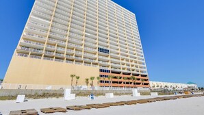 Un hotel de gran altura con varios balcones, una playa de arena frente a él y palmeras.
