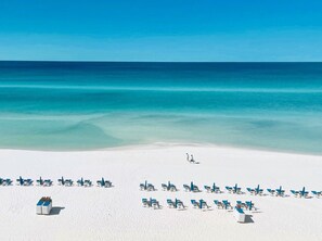A beach with rows of sun loungers and a few people walking.