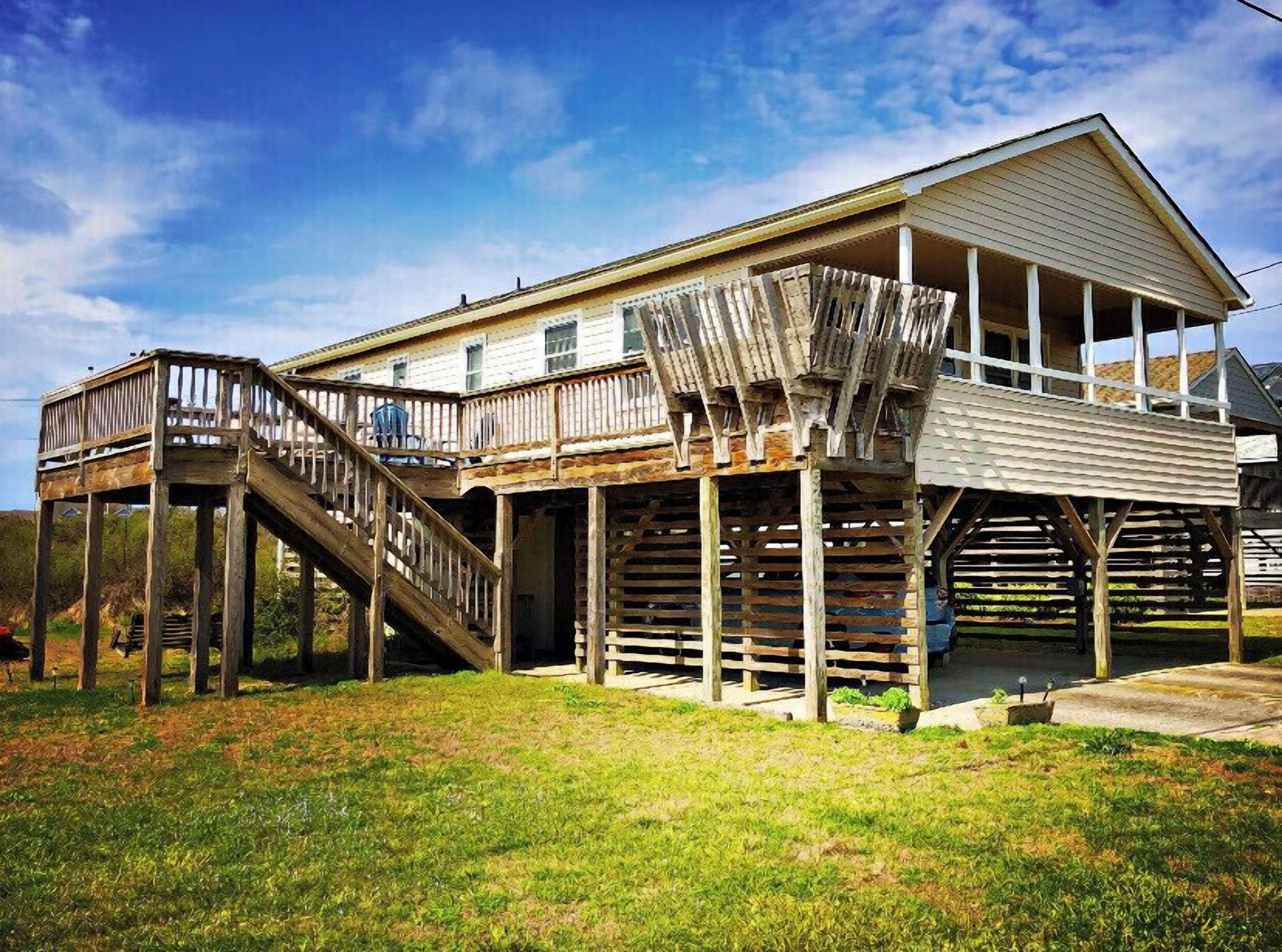 A two-story house with a wooden deck and a staircase leading to the upper floor.