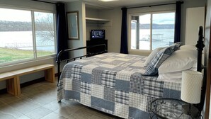 Een slaapkamer met een bed, een bankje, een televisie en uitzicht op een meer.