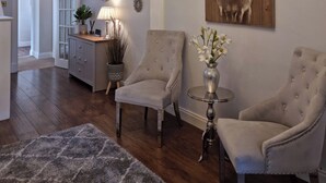 Un salon avec deux fauteuils, une petite table sur laquelle se trouve un vase, une horloge et un tableau accroché au mur.