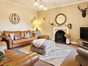 A living room with a brown leather sofa, a grey ottoman, a fireplace, a mounted deer head, and a large clock on the wall. - 5 bedroom accommodation in Scaniport, near Inverness (Scaniport, near Inverness)