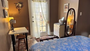 Ein Schlafzimmer mit Bett, Schreibtisch, Stuhl, Kommode, Spiegel und einem Fenster mit Vorhängen.