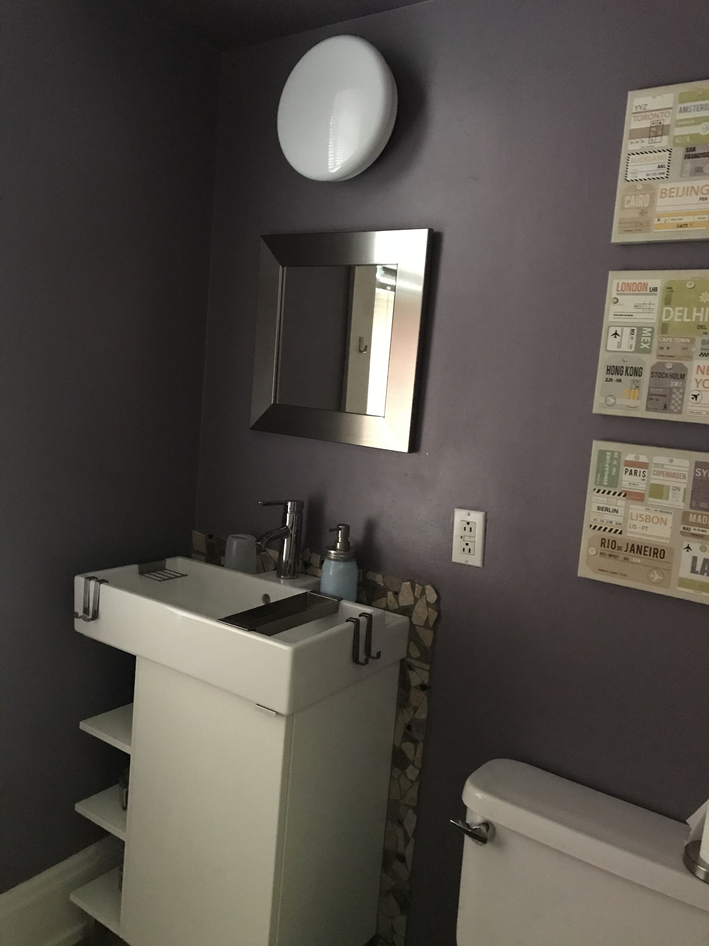 A bathroom with a white sink, mirror, and toilet. There are travel posters on the wall.