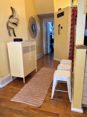 Un couloir avec un plancher en bois, une armoire blanche, un tapis à rayures et un petit tabouret blanc.