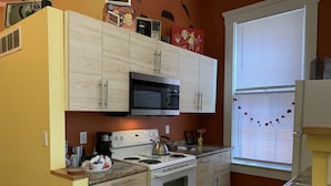 Eine kompakte Küche mit Mikrowelle, Herd und Backofen. Ein Fenster mit Jalousien und ein kleines Waschbecken sind vorhanden.
