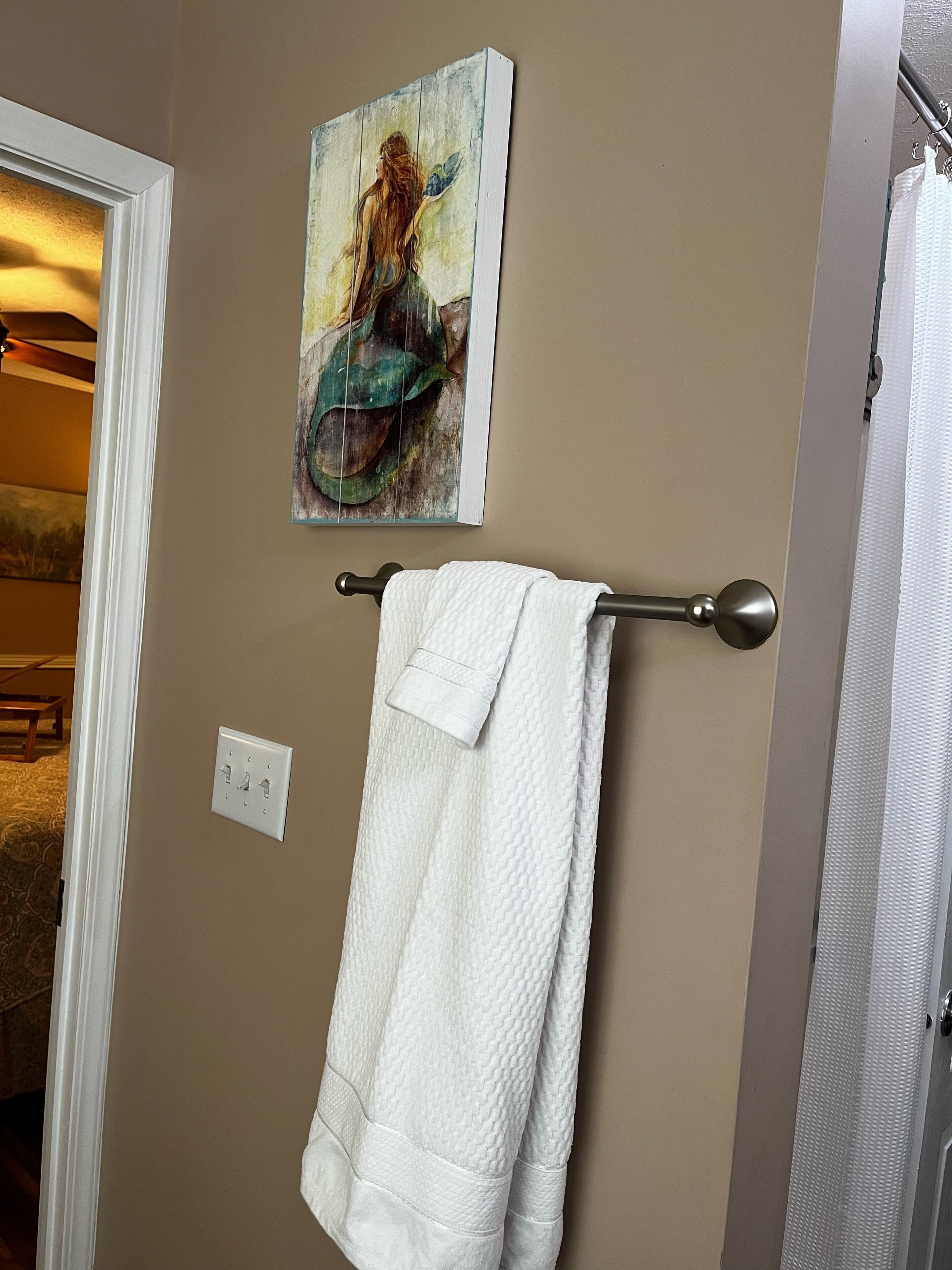 A bathroom with a towel rack holding a white towel, a painting of a woman on the wall, and a visible light switch.