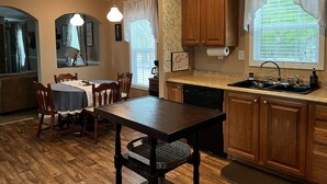 A kitchen with wooden cabinets, a dining table with chairs, a dishwasher, and a window with curtains. - Great property for contract healthcare workers! (Hamlet)