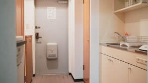 Een smalle gang met een deur naar een kamer, een handdroger en een keuken met een gootsteen en kastjes.