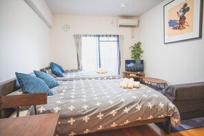 A hotel room with two beds, a TV, a small table, and a plant. - Kyobashi Base (Osaka)