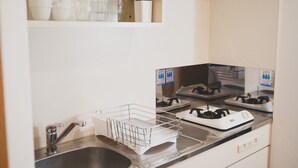 Een keuken met een roestvrijstalen spoelbak, een draadmandenmand, een fornuis en een plank met bekers en bestek.
