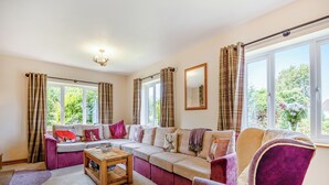 A living room with a sectional sofa, a coffee table, and a chair. There are curtains on the windows, and a chandelier is visible. - 4 bedroom accommodation in Hogsthorpe, near Skegness (Hogsthorpe, near Skegness)