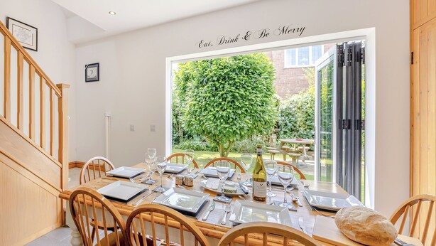 A dining area with a table set for four, a wooden chair, a loaf of bread, and a bottle of wine. - 4 bedroom accommodation in Hogsthorpe, near Skegness (Hogsthorpe, near Skegness)