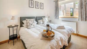 A neatly made bed with a tray of breakfast items, a bedside table with a lamp, and framed artwork on the wall. - 4 bedroom accommodation in Hogsthorpe, near Skegness (Hogsthorpe, near Skegness)