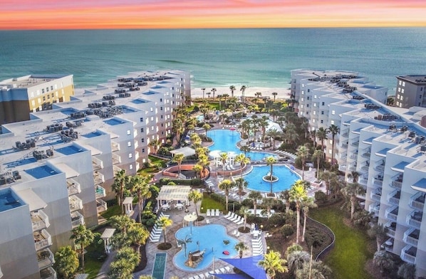 Un resort con varias piscinas, palmeras y vistas a la playa.
