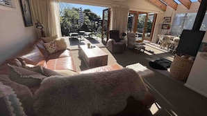 Un salon spacieux avec un grand canapé, une table basse et un téléviseur. Une porte-fenêtre coulissante donne accès à un patio aménagé avec du mobilier d’extérieur.