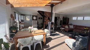 Un vaste espace de vie doté d’un plafond en bois, d’une table à manger avec des chaises blanches, d’un canapé et d’un escalier.