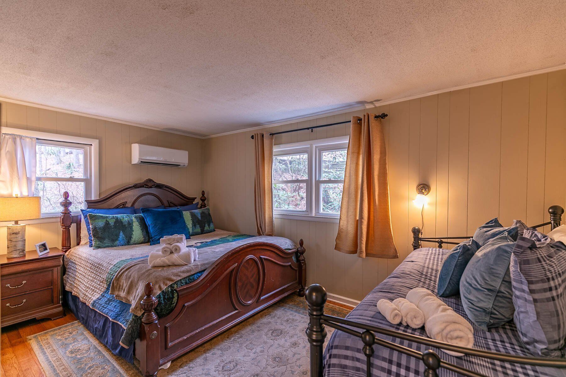 Un dormitorio acogedor con una cama de madera, una mesita de noche, una lámpara y un ventanal con cortinas.