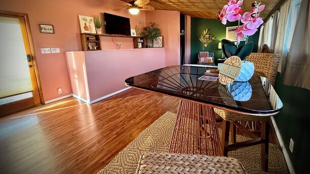 Un salon moderne avec une table basse en verre, un ventilateur de plafond et un mur rose.
