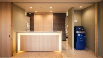 Zona de recepción de hotel con mostrador, una máquina de autoservicio azul y una puerta de madera.