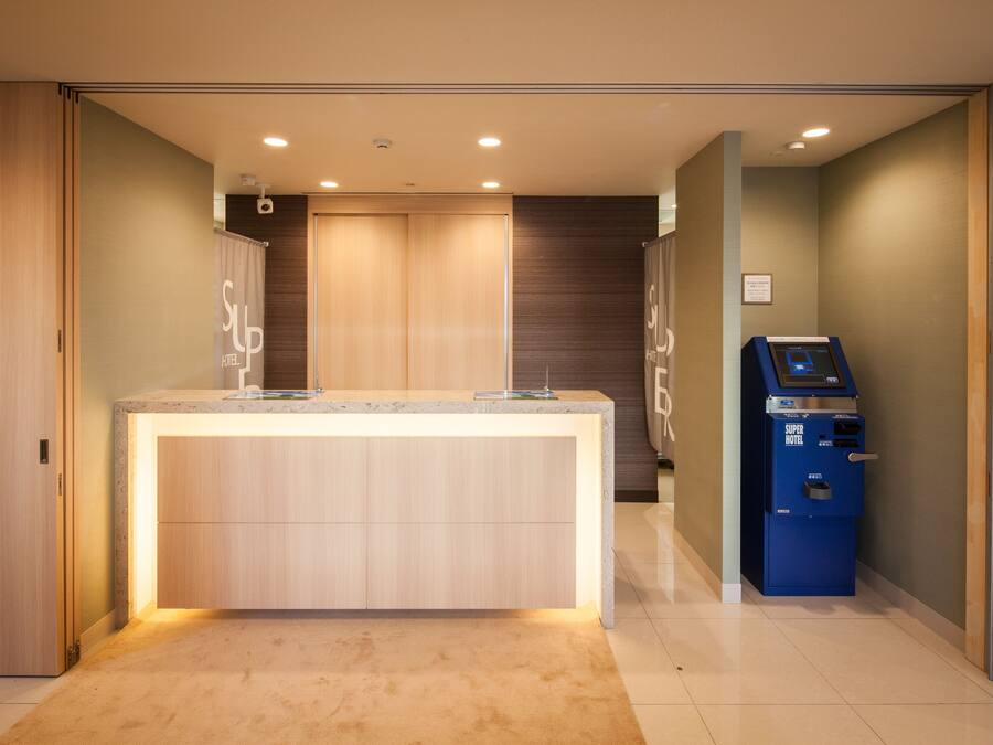 Zona de recepción de hotel con mostrador, una máquina de autoservicio azul y una puerta de madera.