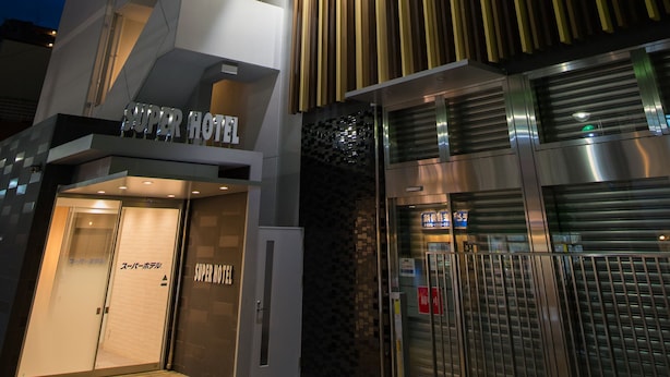 Un hôtel doté d’une façade moderne, de nombreux balcons et d’une enseigne bien visible indiquant qu’il s’agit d’un hôtel de la chaîne Super Hotel.