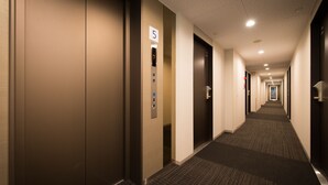Un couloir d’hôtel avec les portes numérotées 5 et 7, un sol recouvert de moquette et un long couloir bordé de portes des deux côtés.