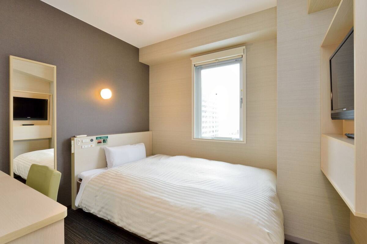 Ein Hotelzimmer mit Bett, Schreibtisch, Wandfernseher und Fenster.