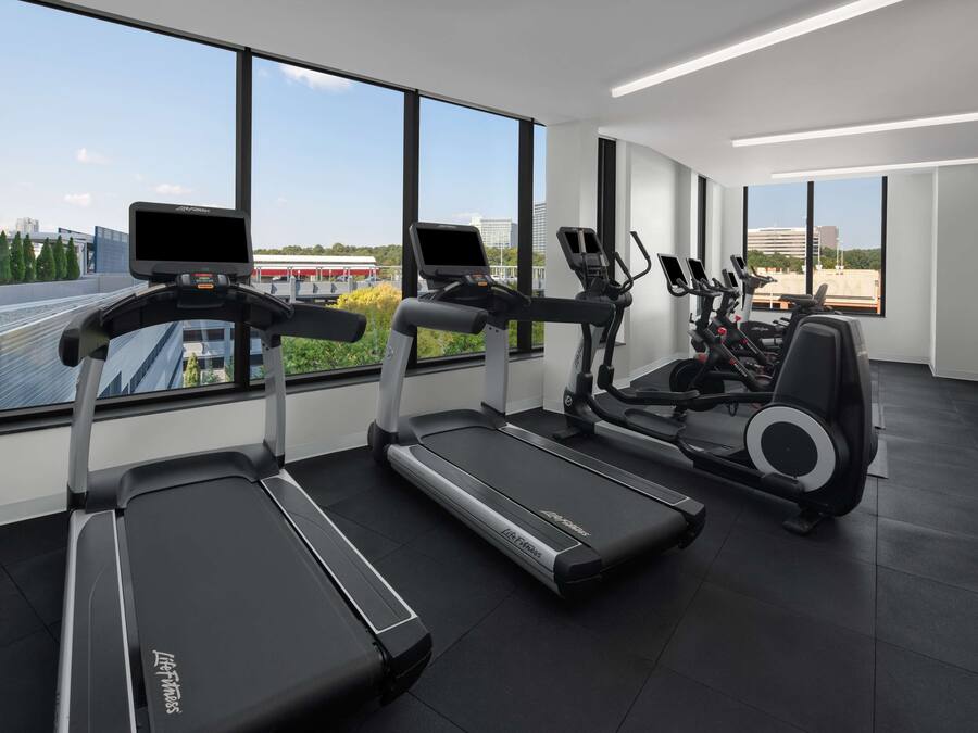 A modern gym with treadmills and elliptical machines, large windows offering a city view.