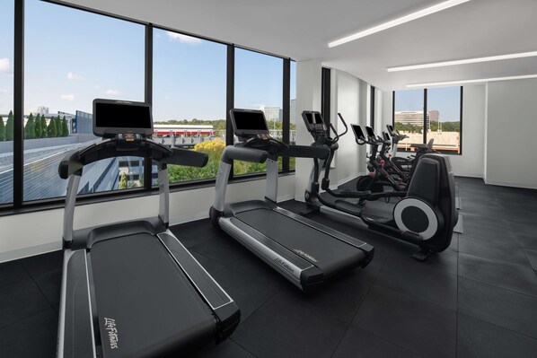 A modern gym with treadmills and elliptical machines, large windows offering a city view.