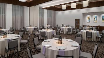 A conference room with multiple round tables, each set with white tablecloths, chairs, and candles.