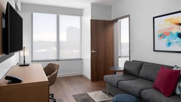 Un salón moderno con un escritorio de madera, un sofá gris y un ventanal con vistas a la ciudad.