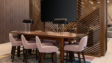 A conference room with a large table, six chairs, two floor lamps, and a large screen.