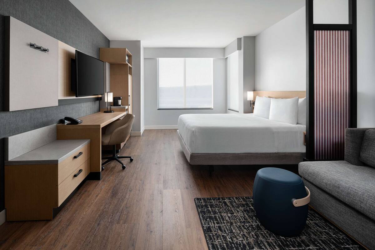 A modern hotel room with a bed, a desk, a TV, and a sofa.