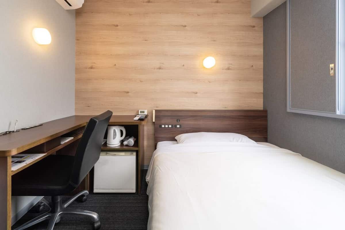 Une chambre d’hôtel avec une tête de lit en bois, un bureau avec une chaise, un lit et un petit coin cuisine.