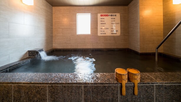 A hot spring bath area with a wooden wall, a tiled floor, and a sign listing amenities. - Super Hotel Ube Kosan Street (Ube)